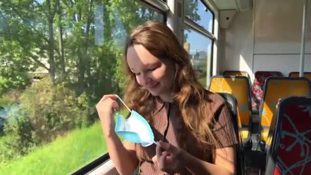 Chica se quita la máscara adolescente pelo castaño en el metro sentado máscara Hay video donde ella se quita y se pone una máscara. camina en tren. muestra la pantalla verde en el teléfono Bailando y sonriendo. — Vídeos de Stock