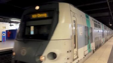 Bir metro treni yeşil ve gri renkli bir trenin yanından geçerken istasyondan istasyona geçerken insanlar görünmez.