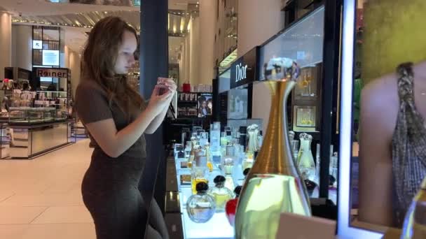 La chica en la tienda huele perfume, ella es hermosa con el pelo castaño suelto en una papilla de una blusa marrón alrededor de una gran cantidad de perfumes diferentes — Vídeo de stock