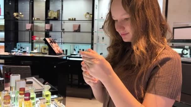Het meisje in de winkel ruikt parfum, ze is mooi met los bruin haar in een pap van een bruine blouse rond veel verschillende parfums — Stockvideo