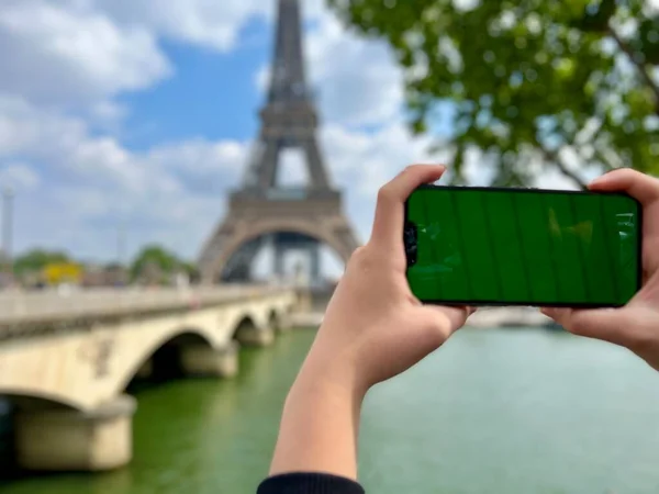 Telefon zöld Chromate képernyővel a háttérben az Eiffel torony. Párizsban használja a mobilját az Eiffel-torony előtt, a kerítőhálós híd háttere, — Stock Fotó