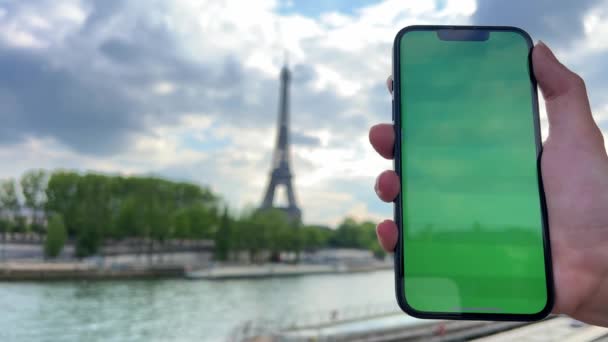 Telefon med grön kromat skärm på bakgrunden av eiffeltornet. i Paris med hjälp av sin mobiltelefon framför Eiffeltornet, snurra bro bakgrund, — Stockvideo