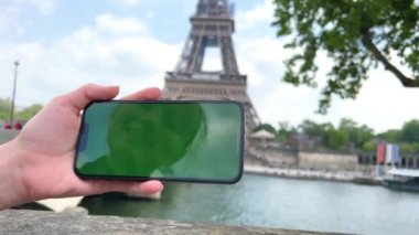 Eyfel Kulesi 'nin arka planında yeşil renkli ekran olan telefon. Paris 'te Eyfel Kulesi' nin önündeki cep telefonuyla, Seine Köprüsü arka planında., 