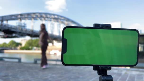 Blank for advertising a travel agency a teenage girl rejoices bouncing against the background of a bridge A in the foreground a phone with a green screen chroma key — 비디오