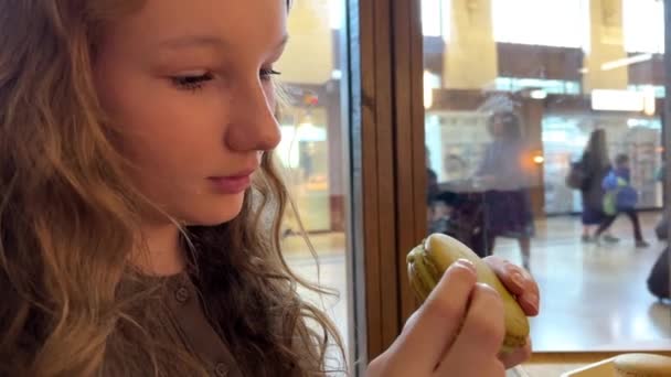 Ein Teenager-Mädchen beißt mit Vergnügen in eine große Pasta, sie mag sie wirklich, es kann eine Werbung für ein Restaurant oder Süßigkeiten sein — Stockvideo