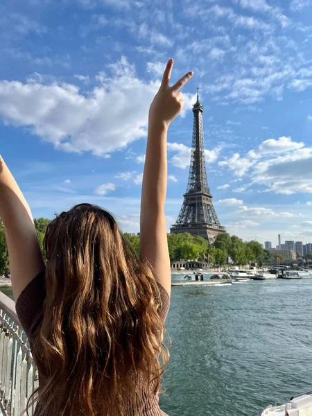 A cheerful teen girl stands against the backdrop of the Eiffel Tower in a beautiful dress, she raised her hand, you can advertise a travel agency trip to Paris France — Stock fotografie