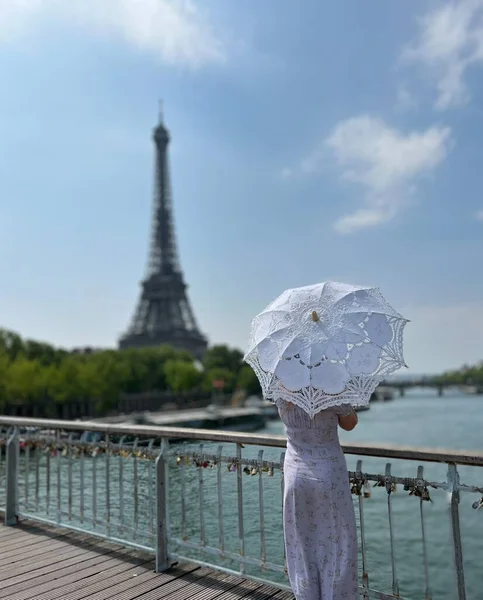 From the back we see a girl in a beautiful long dress with umbrella in a retro style with an umbrella who walks towards the eiffel tower holding the dress with one hand — Stock Photo, Image