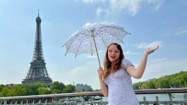 Una chica con una sombrilla blanca se levanta contra el telón de fondo de la Torre Eiffel con su espalda a nosotros se puede utilizar para la publicidad de Internet para las agencias de viajes —  Fotos de Stock