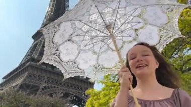 Neşeli bir genç kız Eyfel Kulesi 'nin arka planında güzel bir elbiseyle duruyor. Elini kaldırdı. Paris' e seyahat acentesinin Fransa 'ya yaptığı gezinin reklamını yapabilirsiniz.