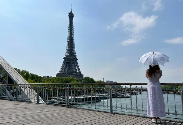 Ein schönes Teenagermädchen blickt in das Gestell, das vor der Kulisse des Eiffelturms lehnt Sie lächelt und scheint hier großartige Werbung für eine Reise nach Paris zu machen — Stockfoto