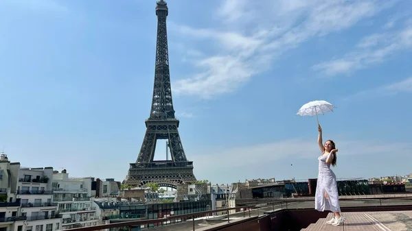 A beautiful young girl dances and spins near the Eiffel Tower with an openwork sun umbrella she is happy rejoices can be used for any advertising for any joy and happiness — Stok fotoğraf