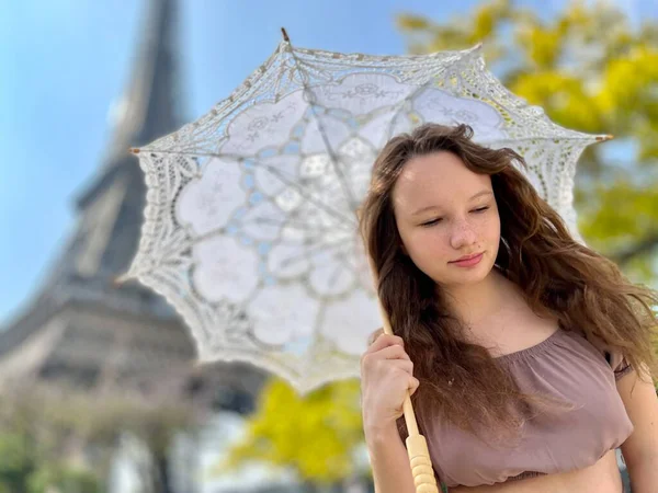 Uma menina com um guarda-sol branco está contra o pano de fundo da Torre Eiffel com suas costas para nós pode ser usado para publicidade para a Internet para agências de viagens — Fotografia de Stock