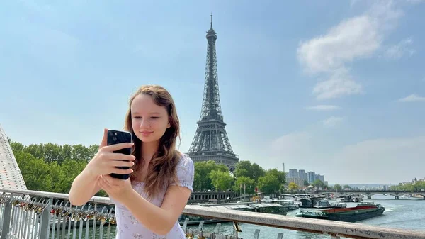 Flickan är upptagen på telefonen hon tittar på något på Internet vid denna tid hon står med ryggen till Eiffeltornet hon är i en vacker sommar klänning milt ljus — Stockfoto