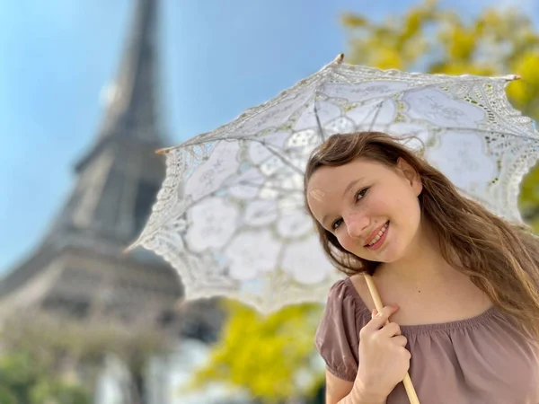 A beautiful teenage girl looks into the frame leaning against the backdrop of the Eiffel Tower She smiles and seems to be showing come here great advertisement for a trip to Paris — стоковое фото