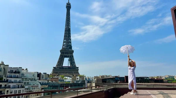 Dívka s bílým slunečníkem stojí na pozadí Eiffelovy věže zády k nám může být použita pro reklamu na internet pro cestovní kanceláře — Stock fotografie