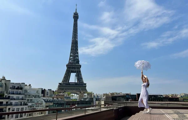 Girl in a blue dress stands on the background of the Eiffel Tower a lot of space for text she is happy in her hands holding a sun umbrella raising her hands Up looks like Mary Poppins — Stock Photo, Image