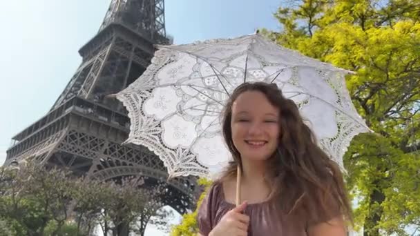 A cheerful teen girl stands against the backdrop of the Eiffel Tower in a beautiful dress, she raised her hand, you can advertise a travel agency trip to Paris France — Stockvideo
