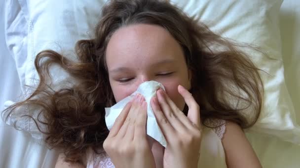 Las niñas tienen una secreción nasal se sopla la nariz una servilleta blanca tiene un resfriado o una alergia estacional se acuesta en la almohada su pelo está suelto cama blanca — Vídeos de Stock