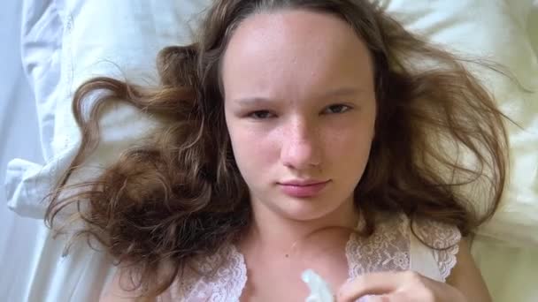 Chica adolescente enojado lanza servilletas a la cámara que es infeliz se encuentra en la almohada mira en el marco. Alta calidad 4k — Vídeos de Stock