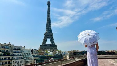 a beautiful young girl in a summer dress stands against the backdrop of the Eiffel Tower with a lace umbrella, she raised her hand and as if taking off there is a place for advertising travel agency