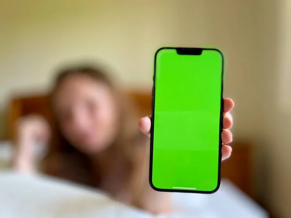 The girl smiles lies in her bed and shows the phone with a green screen can be used to advertise seasonal allergies or colds When the girl has already recovered — Stock fotografie