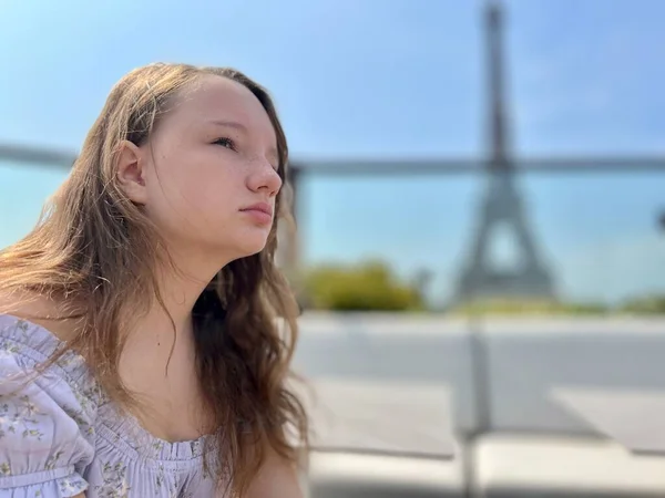 The face of a girl who sits against the backdrop of the Eiffel Tower she is thoughtfully relaxed beautiful there is a place for text for advertising — Stock Fotó