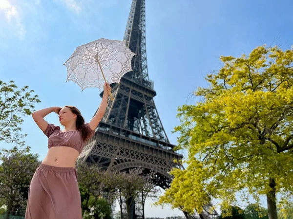 Blue picture blue sky blue dress a slender girl with an openwork umbrella stands near the Eiffel Tower and opens the umbrella looks at her — Foto Stock