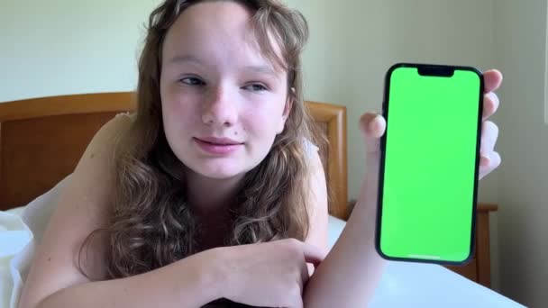女の子の笑顔は彼女のベッドにあり、緑の画面で携帯電話を示しています季節のアレルギーや寒さを宣伝するために使用することができます女の子がすでに回復したとき — ストック動画