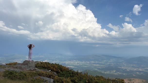 Na najwyższej górze Portugalii stoi dziewczyna, której włosy wieją na wietrze stojąc na szczycie góry, relaksując się i ciesząc pięknym letnim krajobrazem górskim. Widok panoramiczny — Wideo stockowe