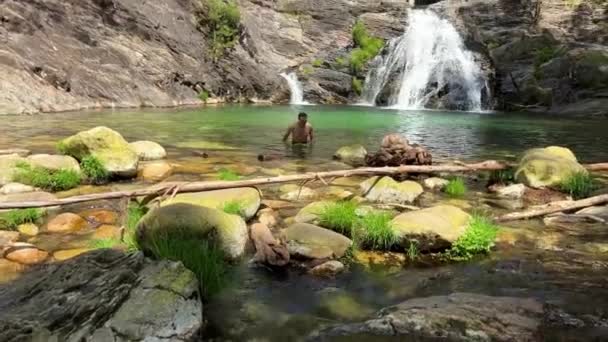 Bonito sexy escuro-haired homem como Tarzan sai de um montanha rio perto de um cachoeira filmagem como se de um aventura filme — Vídeo de Stock