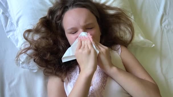 Een tienermeisje ligt op een wit kussen, snuit haar neus met een witte servet, ze heeft een verkoudheid of een seizoensgebonden allergie — Stockvideo