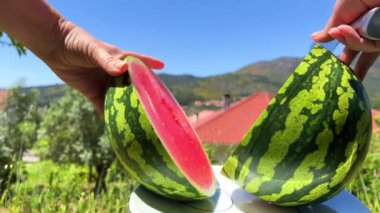Bir kadın bir karpuz keser ve karpuz, dağların arka planına karşı iki parçaya ayrılır. Çok parlak ve sulu bir çerçeve.