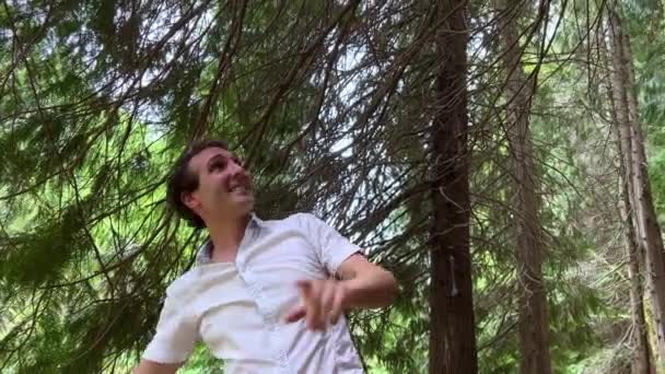 Un francés o un español levanta 2 manos arriba se inclina hacia adelante muestra los dedos en una dirección que sonríe está en el bosque en una camisa blanca — Vídeos de Stock