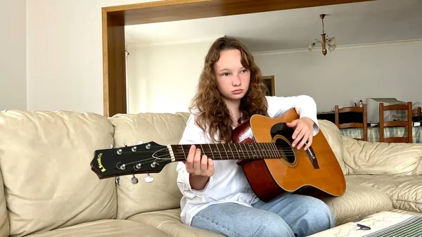 Светловолосая девушка в белой рубашке и джинсах сидит с гитарой, на которой она не играет — стоковое фото