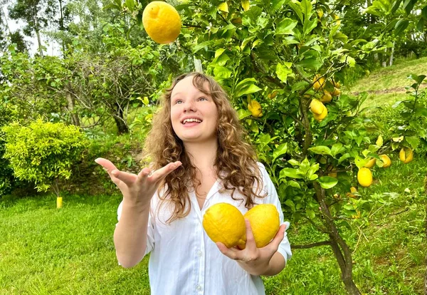 Chica adolescente divertirse bailando sonrisas y se ríe en el telón de fondo de un limonero en sus manos ella tiene limones ella tontos alrededor con ellos —  Fotos de Stock