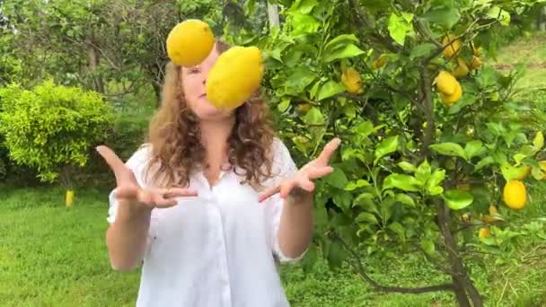 Девочка-подросток весело танцует улыбается и смеется на фоне лимонного дерева в ее руках она имеет лимоны она дурачится с ними — стоковое видео