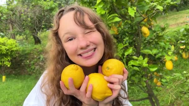 Девочка-подросток весело танцует улыбается и смеется на фоне лимонного дерева в ее руках она имеет лимоны она дурачится с ними — стоковое видео