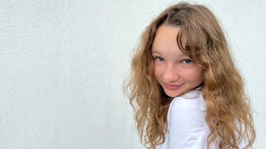 Beyaz bir arka planda beyaz bir kız, açık renk saçlı, farklı duygular besliyor, yüzler yapıyor, mutlu bir şekilde gülüyor, saçlarını dalgalandırıyor ve dilini gösteriyor.