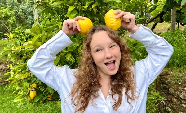 Ragazza adolescente divertirsi ballando sorrisi e ride sullo sfondo di un albero di limone nelle sue mani lei ha limoni lei scherza intorno con loro — Foto Stock