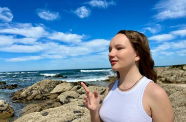 Beyaz bluzlu bir kız, açık renk saçlı, farklı duygular besliyor, yüzler yapıyor, mutlu bir şekilde gülüyor, saçlarını dalgalandırıyor ve dilini gösteriyor. Yüksek kalite fotoğraf