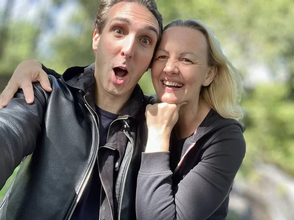 cheerful adult French man and blonde woman making faces surprised and laughing looking at the camera they are dressed in black close-ups of faces and emotions they are about 35-45 years old.