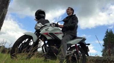 Motosikletli bir erkek, doğanın arka planına karşı bir motosiklete biner ve dağ motosikletinin gidonunda deri bir ceket giyer ve kask takar. Yüksek kalite fotoğraf