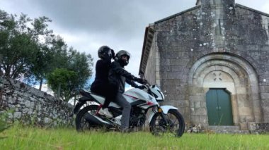 Bir adam ve bir kadın siyah giyinmiş ve kafalarında motosiklet kaskı var. Beyaz bir motosiklete biniyorlar ve kadının arka direksiyonuna biniyorlar. Yüksek kalite 4k