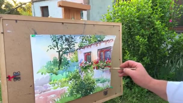 45岁至55岁的成年男性画家画一幅图画 看着他面前的房子 上面有一张纸 你已经可以看到窗户和绿色的木头 还有许多油漆和刷子 — 图库视频影像