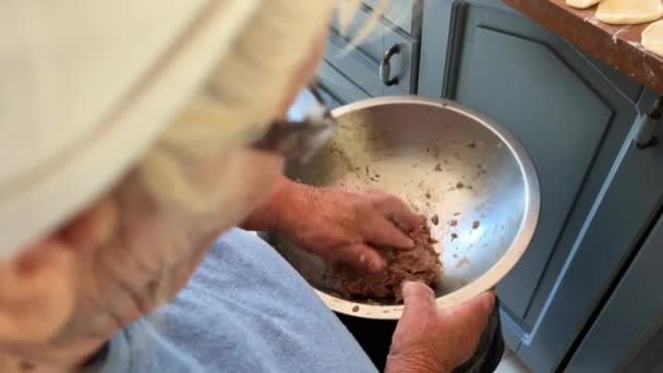 80年の愛を持って祖母は家族の守護者である餃子を準備し 白いスカーフと青いジャケットを着て 彼女は台所に座って 餃子と餃子の揺れを彫刻します — ストック動画