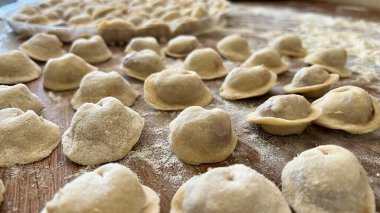  Hamur köftelerini heykeller ve ahşap bir masaya koyar, onlardan bir sürü vardır, unu iştah açıcıdırlar ve pişirilmeyi beklerler her hamur köftesi etle doludur, yuvarlaktır ve düzgünce el yapımıdır.