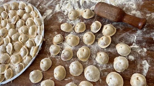 Sculpts dumplings and puts them on a wooden table, there are a lot of them, they are appetizing in flour and waiting to be cooked Each dumpling is full of meat, they are round and neatly handmade