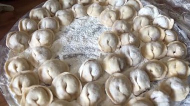  Hamur köftelerini heykeller ve ahşap bir masaya koyar, onlardan bir sürü vardır, unu iştah açıcıdırlar ve pişirilmeyi beklerler her hamur köftesi etle doludur, yuvarlaktır ve düzgünce el yapımıdır.