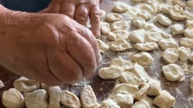  Hamur köftelerini heykeller ve ahşap bir masaya koyar, onlardan bir sürü vardır, unu iştah açıcıdırlar ve pişirilmeyi beklerler her hamur köftesi etle doludur, yuvarlaktır ve düzgünce el yapımıdır.