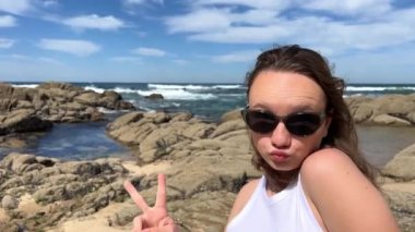 Beyaz bluzlu, açık renk saçlı bir kız, farklı duygular gösterir, suratını asar, mutlu bir şekilde güler, saçlarını dalgalandırır ve dilini gösterir. Yüksek kalite 4k görüntü